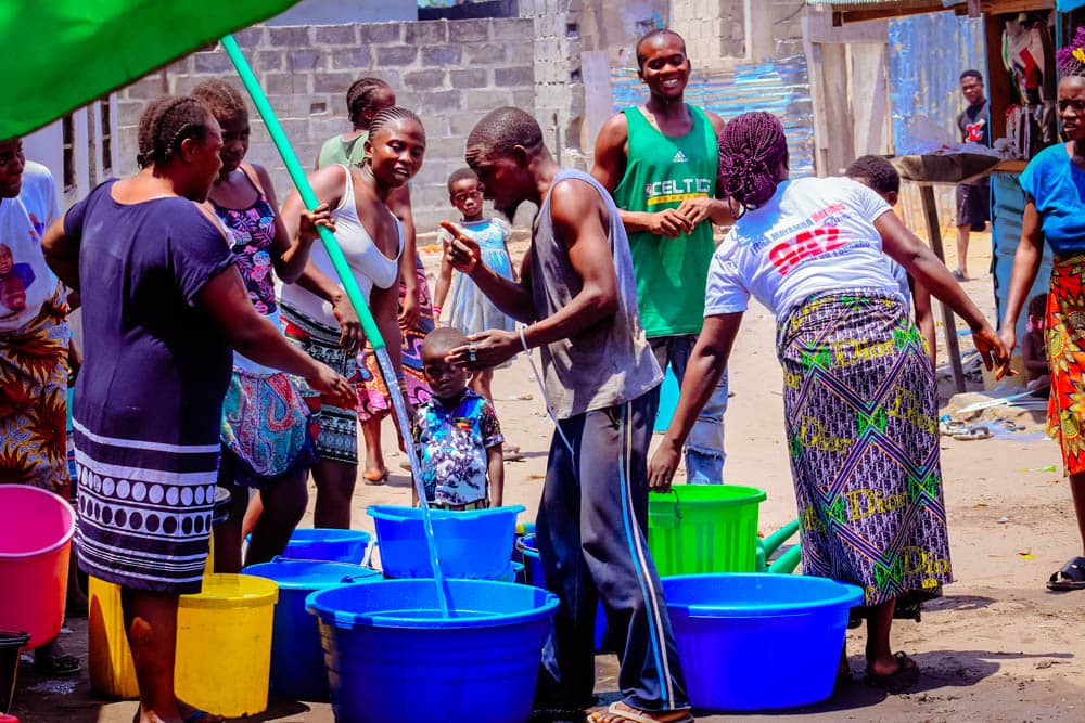 Families collecting clean water from a community hose into buckets